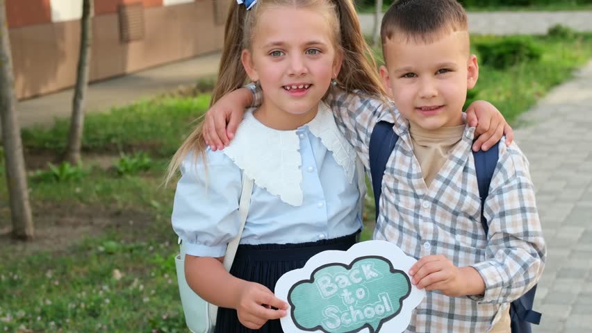 back to school. A girl and a boy, schoolchildren at the school hold a sign with the inscription back to school, joyful first-graders brother and sister with briefcases rejoice at the first school day