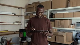 Medium portrait of black male warehouse worker filling delivery document and smiling at camera - Powered by Shutterstock - Get 15% off with code: PIKWIZARD15