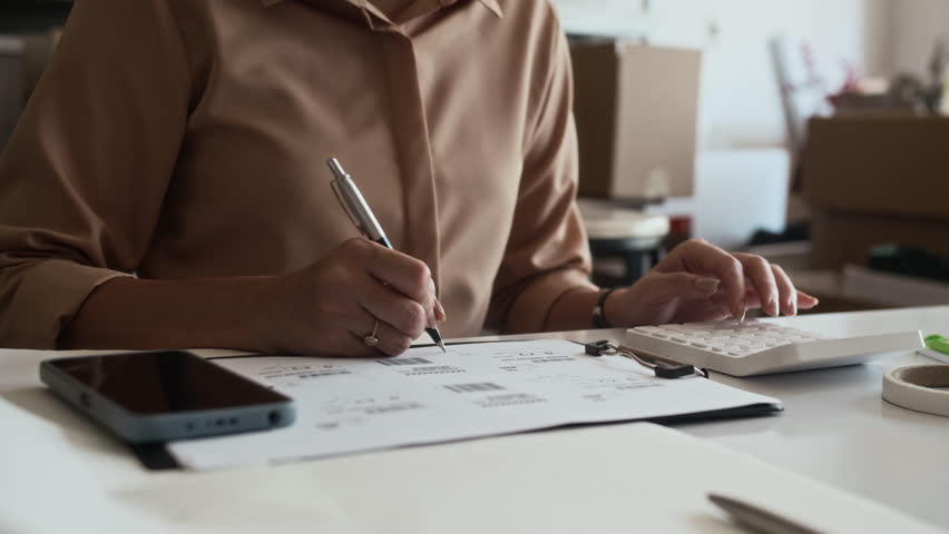 Cropped shot of unrecognizable female worker calculating and filling documents on desk at storage office