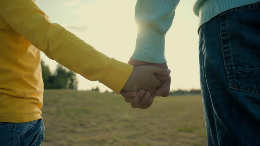 Close up unrecognizable Caucasian family male man father parent dad holding hands little boy child son kid arm bonding closeness support happy childhood teamwork fatherhood outside rural meadow field