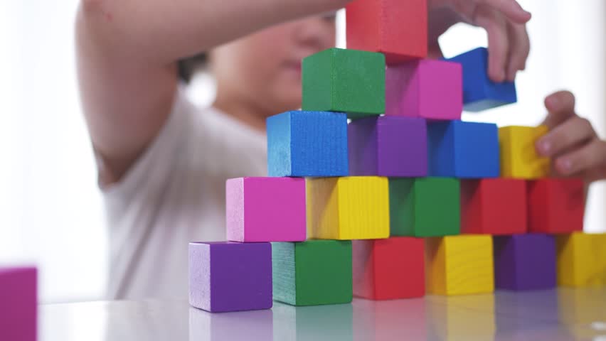 A girl plays with blocks and toys in kindergarten. Constructor little child concept. The girl daughter is playing with cubes. Girl lifestyle collects toys from a stack of cubes.