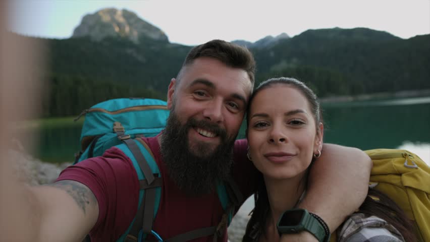 Cheerful couple with backpacks taking a selfie during a mountain hike with a scenic view. Happy Couple Taking Selfie on Mountain Hike