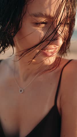 Close up portrait of beautiful brunette woman smiling on the beach during a golden sunset