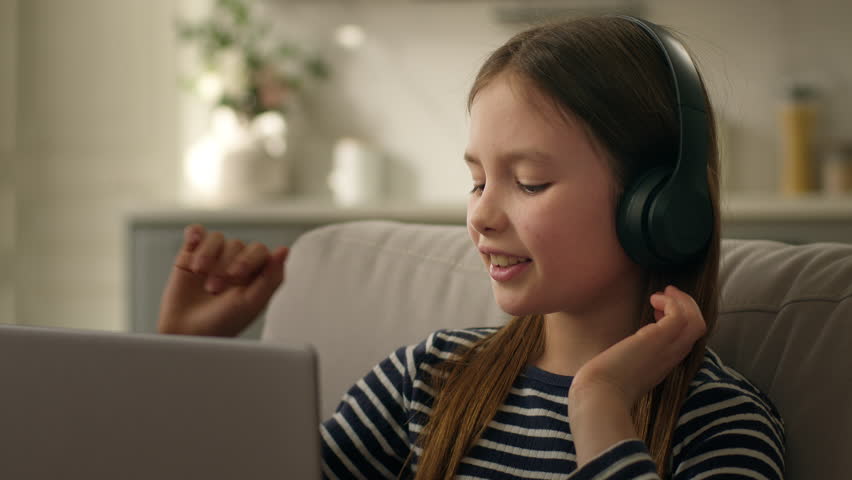 Little Caucasian girl headphones laptop computer technology web cyberspace listen music joy pastime home weekend leisure electronic device audio childhood dance earphones emotion enjoy fun happy smile