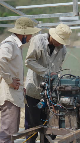 three Vietnamese mechanics repairing and welding an old boat engine