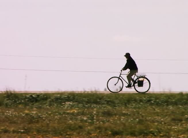 The elderly person goes on a bicycle on rural steppe road on a background of the