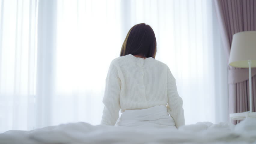 Young Asian Woman stretching in bed after waking up, back view, happy female and relaxed after good night sleep. Sweet dreams, good morning, new day, weekend, holiday, cozy and comfort
