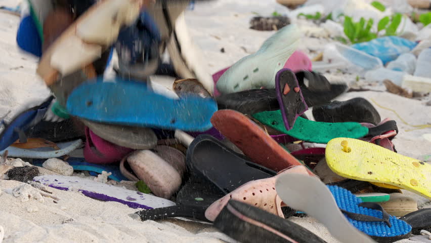 Discarded flip-flops, footwear, or sandals falling on a sandy beach, plastic waste and marine pollution