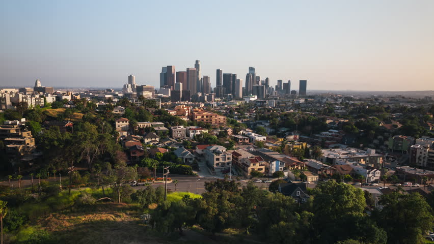 Aerial view of Los Angeles, CA, iconic downtown skyline on a sunny day, Skyscrapers rise against the clear blue sky, with palm-lined streets and the expansive urban landscape bathed in California sun
