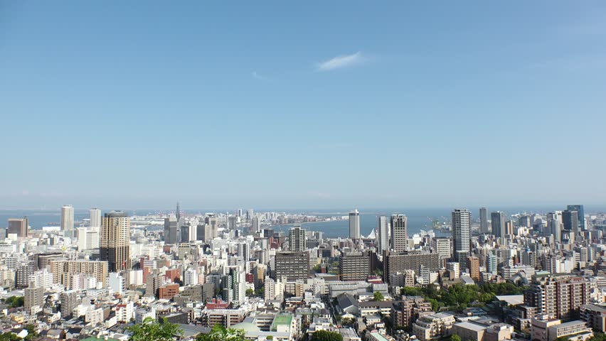 KOBE, HYOGO, JAPAN - JUNE 2024 : Aerial high angle view of Kobe city and Kobe port in daytime. View of buildings and street around Kobe port tower and Sannomiya station. 4K time lapse shot.