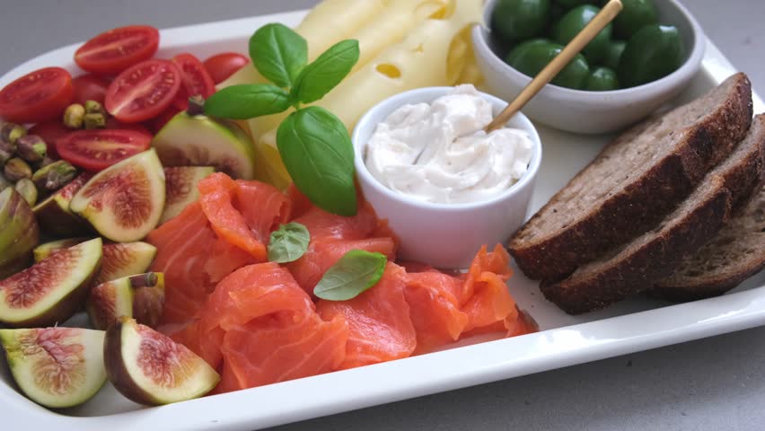 Salmon, cheese, olives, bread and vegetables breakfast platter, white background.