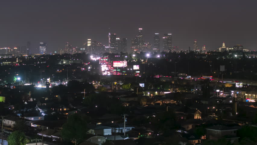 Aerial view of Los Angeles at night, showcasing the iconic downtown skyline, city lights shimmer against the dark evening sky, with skyscrapers glowing brightly and the sprawling urban landscape