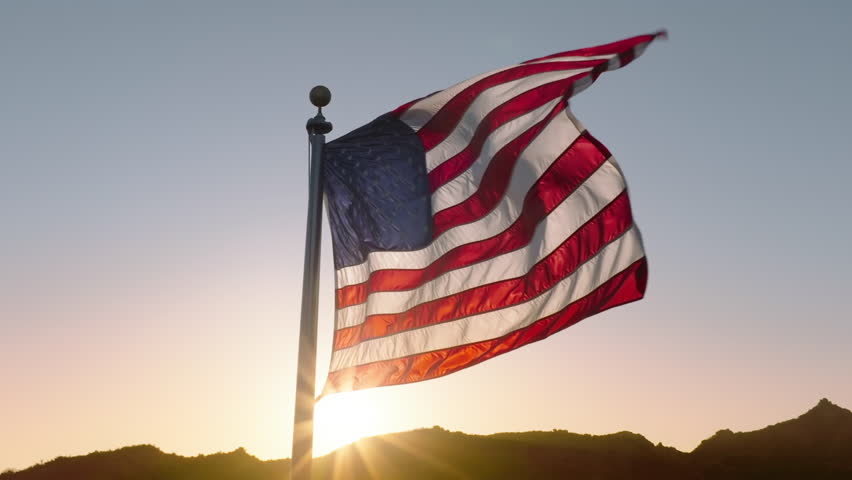 A 4K aerial view of the American flag waving proudly against the backdrop of a sunset, representing patriotism, independence, and national pride, ideal for July 4th and Presidents' Day.