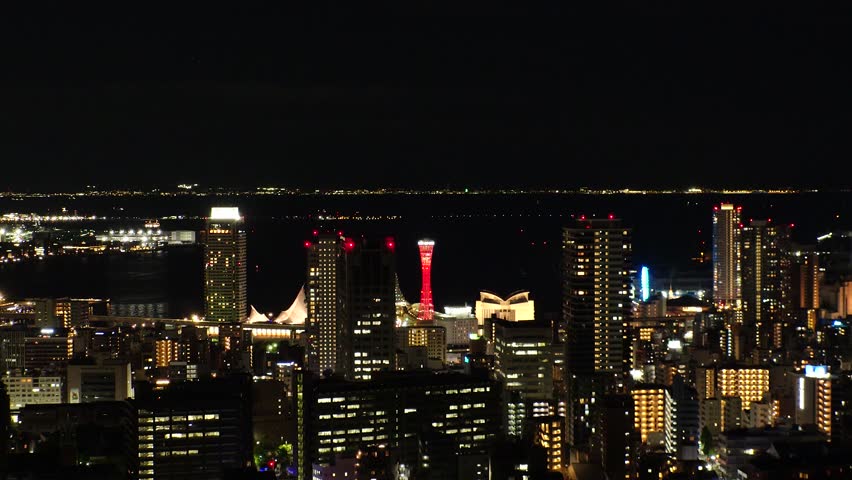 KOBE, HYOGO, JAPAN - JUNE 2024 : Aerial high angle view of Kobe city and Kobe port at night. View of buildings and street around Kobe port tower and Sannomiya station. 4K time lapse shot.