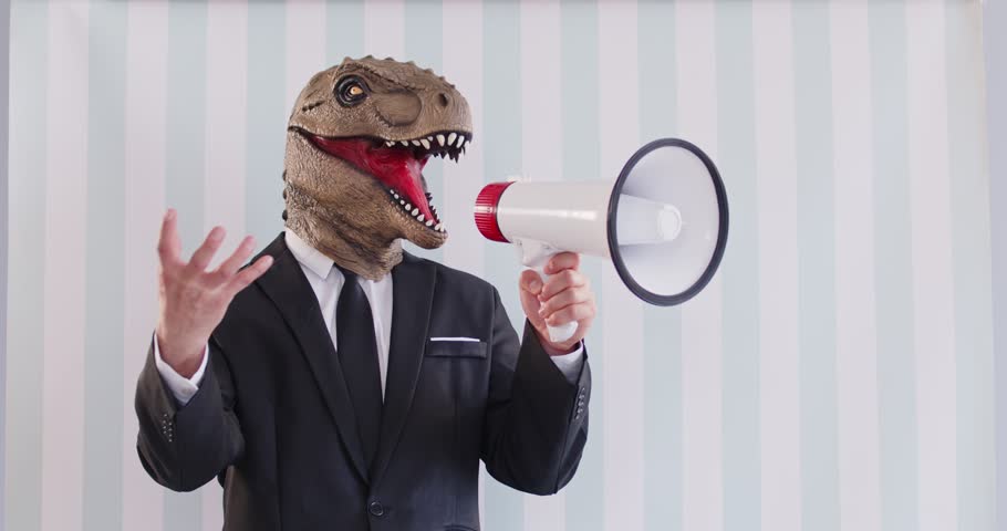 Politician in dinosaur mask creative costume on striped light backdrop makes PR noise speech in megaphone voice amplifier gesticulates promotes idea. Leadership team manager motivates employee to work