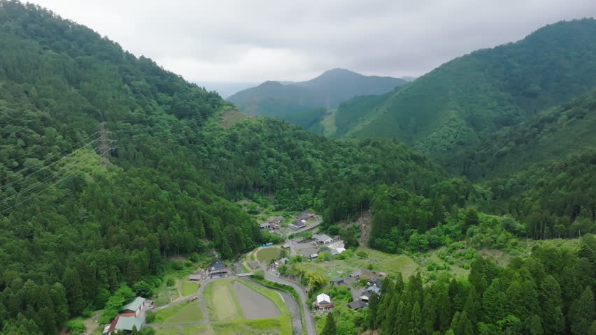 Flying away from small village in lush green mountains of Japan