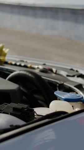Mechanic poured antifreeze in car cooling system repair at auto repair shop. Male technician works under the hood of the customer's car at a car service. Vertical video for story