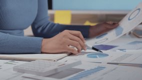 Businesswoman analyzes financial reports, uses a calculator, and takes notes in an organized office setting with charts and graphs on the desk - Powered by Shutterstock - Get 15% off with code: PIKWIZARD15