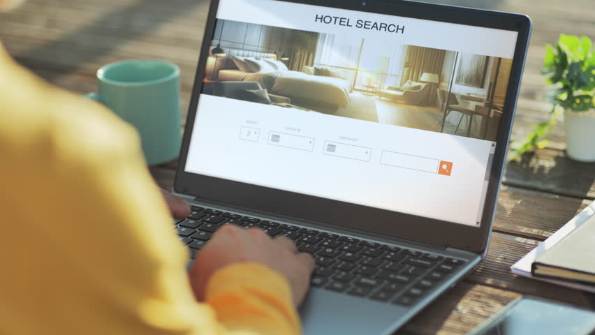 back view of man at computer doing hotel room research on the web,male at the laptop planning vacation searching for hotels accommodation online on the internet website