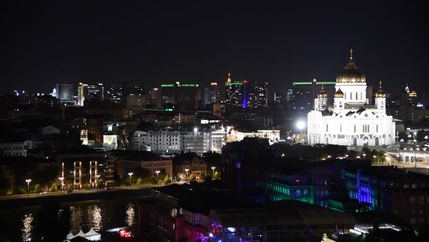 High angle night cityscape of downtown district with white illuminated Russian Orthodox Cathedral of Christ the Saviour on river embankment in Moscow, Russia. Rare cars drives on road.