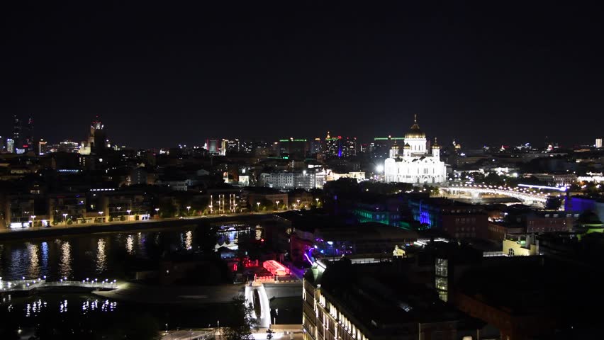 High angle night cityscape of downtown district with white illuminated Russian Orthodox Cathedral of Christ the Saviour on river embankment in Moscow, Russia. Rare cars drives on road.