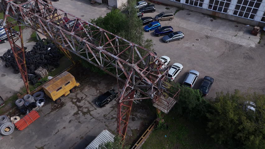 Aerial View of Abandoned Industrial Crane and Equipment. Drone shot of rusty crane surrounded by tires and trailers.