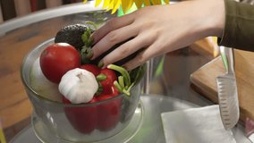 Woman is choosing a vegetable from the bowl and taking tomato to cut it on the wooden board. Closeup of female hands cooking guacamole sauce from ripe and fresh organic products. Nourishment theme - Powered by Shutterstock - Get 15% off with code: PIKWIZARD15