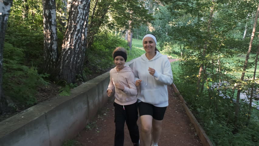 Woman and her daughter joyfully run together on a sunlit path at dawn, enjoying the natural surroundings and their time together, slow motion. Healthy lifestyle