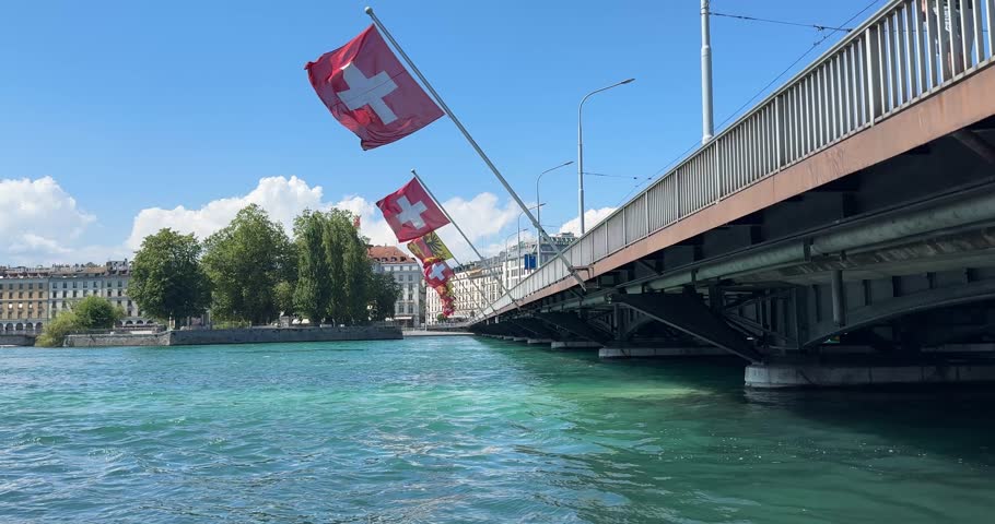 Swiss flag blows in the wind in Geneva at Mont Blanc Bridge at Lake Geneva on a sunny summer day