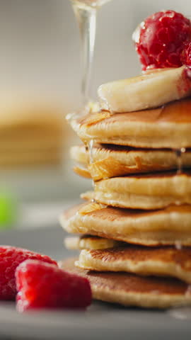 Portrait Screen. Dessert, cook pouring honey over pancakes with berry assortment in modern culinary space. Applying honey to pancakes with fruits, uses variety ingredients from berries, pancake baking