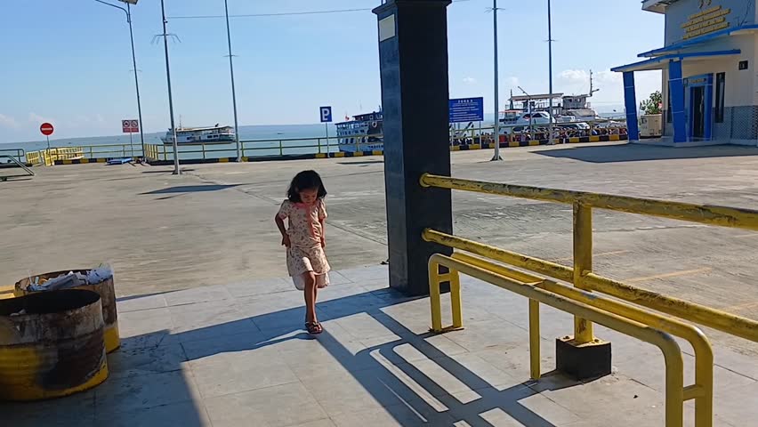a little Asian girl plays with the shadow of the guardrail at the harbor in the afternoon