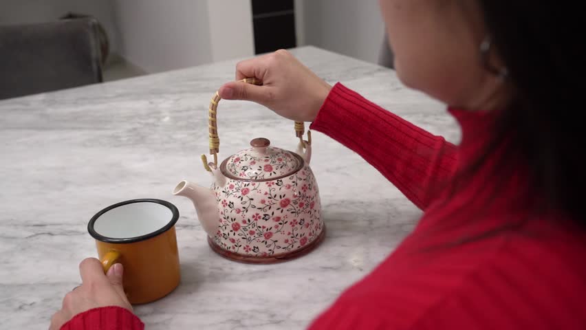 Teatime. Over shoulder shot view of a woman hands holding a kettle and pouring tea into a cup. 