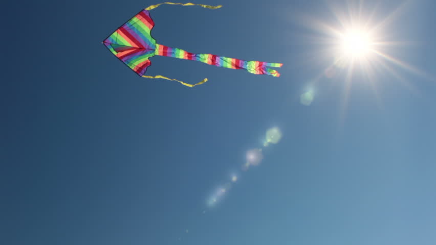 A kite flies against the bright blue cloudless sky. The sun is shining brightly.