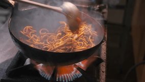 Cooking stir-fried noodles with vegetables and meat on high heat with shaking and stirring with steel ladle in commercial kitchen, close up. - Powered by Shutterstock - Get 15% off with code: PIKWIZARD15