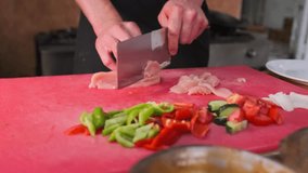Hands of a male chef cutting thin slices of chicken fillet for frying next to chopped vegetables onions bell peppers and tomatoes with cucumber. - Powered by Shutterstock - Get 15% off with code: PIKWIZARD15