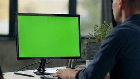 Young Man Working In Office On Desktop Computer with Green Screen Mock Up Display. Over the Shoulder- Close-up of Monitor With Green Screen Chromakey - Powered by Shutterstock - Get 15% off with code: PIKWIZARD15