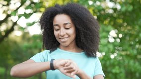 Happy young african american female looking smart watch in urban city park. Sportswoman using checking fitness tracker. Fit black woman is satisfied with the results of training, rejoices. Close up - Powered by Shutterstock - Get 15% off with code: PIKWIZARD15