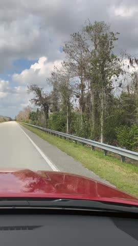 Driving along the Tamiami Trail through the Everglades in Florida, capturing the scenic landscape, wetlands, and forested areas under a partly cloudy sky