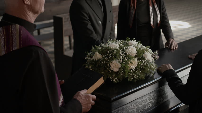 High angle view of four people keeping hands on coffin lid while senior priest performing funeral service in church