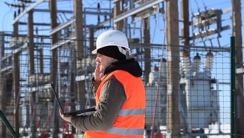 Electrician with computer near the electricity substation