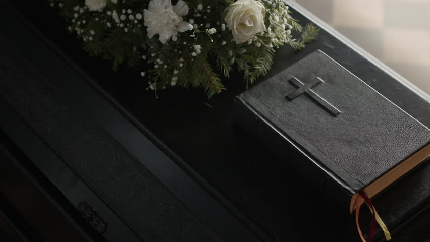 Close up no people view of coffin lid with white flowers and holy bible at funeral ceremony in cathedral