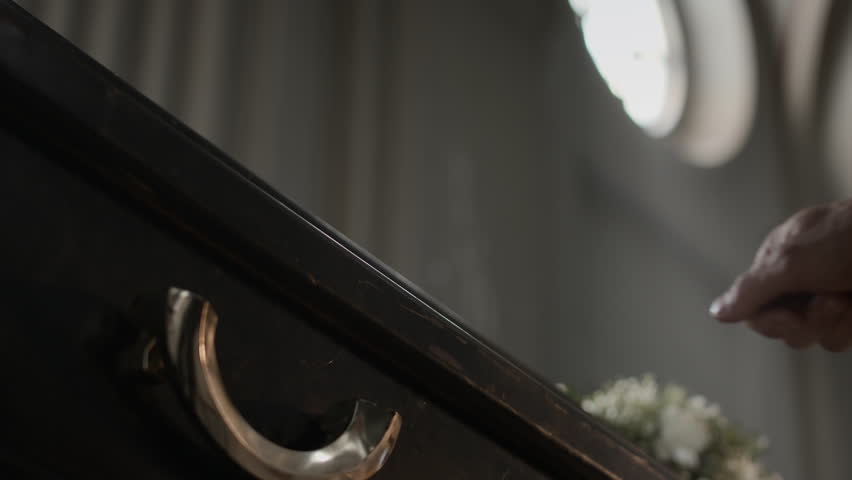 Low angle view of unrecognisable man passing hand over coffin lid and removing it slowly at church funeral service