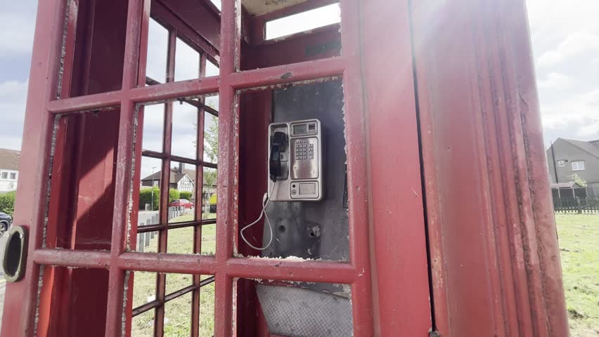 Classic British iconic Red Telephone box, unloved, smashed and vandalised. Eltham Palace Road, London. A telephone handset is places on the receiver, or a smashed, vintage red British telephone box.