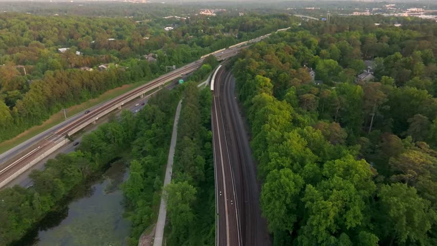 Drone shot of Atlanta metro rail crossing through natural park trails of Buckhead neighbourhood, Georgia State Route 400, T Harvey Mathis Parkway