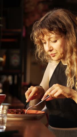 Woman enjoying breakfast at a cafe, close-up of face and hands cutting pancakes with fork and knife. Girl has breakfast with gluten-free oatmeal pancakes with berries and chocolate cream.