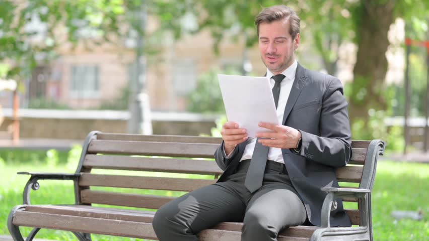 Middle Aged Businessman Celebrating while Reading Documents Outdoor