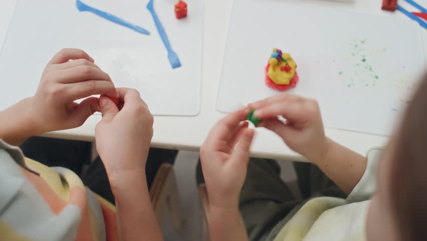 Top view of unrecognizable preschool children learning how use modelling clay by rolling and kneading small playdough pieces in hands during art lesson