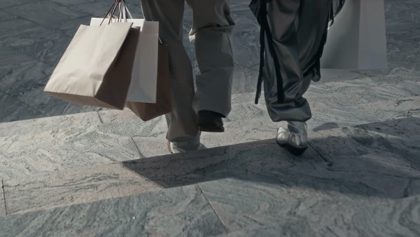 Back view of fancy celebrity couple walking towards expensive black car, giving paper shopping bags to Asian driver and getting inside