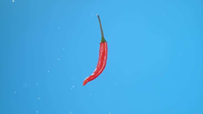 Single small hot red chili pepper flying through air and spinning with small water droplets. High quality cinematic studio commercial super slow motion 1000fps fresh pepper moving up and down. - Powered by Shutterstock - Get 15% off with code: PIKWIZARD15