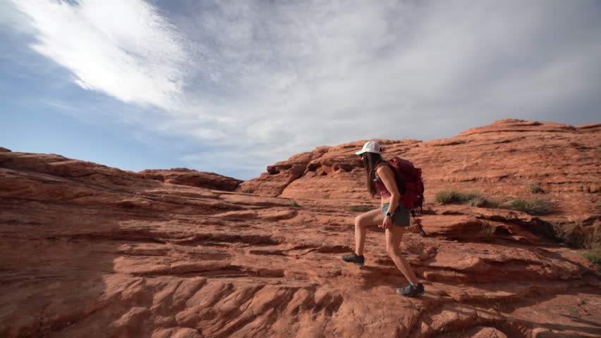 Young Woman With Backpack Walking on Red Sandstone Hills on Hot Sunny Day